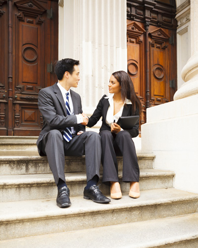 Lawyer and client shake hands while sitting on the steps of a state court building.